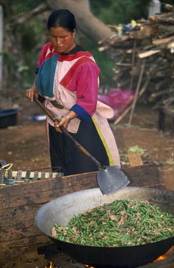 THAILAND, Chiang Rai Province, Huai Khrai, Lisu woman stir frying meal in large wok for New Year dinner