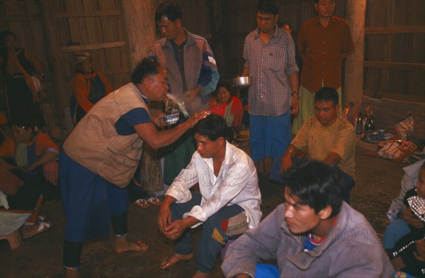 THAILAND, Chiang Rai Province, Doi Lan, Lisu shaman spraying supplicants head at healing ceremony
