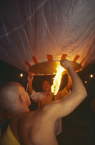 THAILAND, Chiang Mai, Mae Jo San Sai District, Loi Krathong Festival aka Yi Peng. Monk and another man launching hot air balloon into the night sky