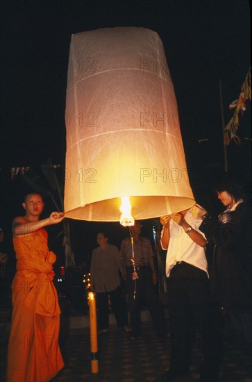 THAILAND, Chiang Mai, Wat Chaimongkon, Loi Krathong Festival aka Yi Peng. Monk and other people launching hot air balloon into the night sky