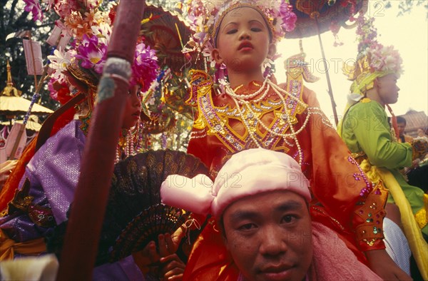 THAILAND, Chiang Mai, Shan Poi San Long. Crystal Children ceremony with Luk Kaeo in costume sitting on mans shoulders at Wat Pa Pao