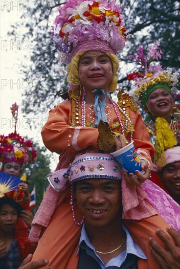 THAILAND, Chiang Mai, Shan Poi San Long. Crystal Children ceremony with Luk Kaeo in costume sitting on mans shoulders at Wat Pa Pao