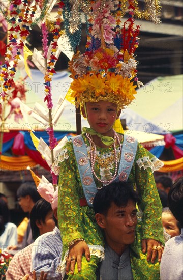 THAILAND, Chiang Mai, Shan Poi San Long. Crystal Children ceremony with Luk Kaeo in costume sitting on mans shoulders at Wat Pa Pao