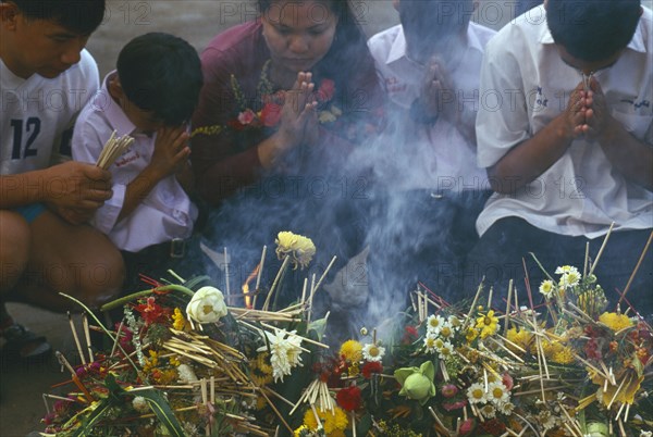 THAILAND, Chiang Mai, Wat Jedi Luang, Inthakhin Ceremony. People praying in front of offerings of flowers and joss sticks