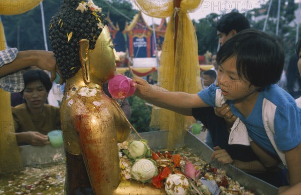THAILAND, Chiang Mai, Wat Jedi Luang, Inthakhin Ceremony. Young boy bathing Phra Fon Saen Ha Buddha statue surrounded by floral offerings and pool