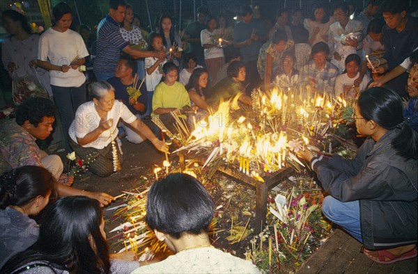 THAILAND, Chiang Mai, Wat Jedi Luang, Inthakhin Ceremony. People lighting candles on offerings table