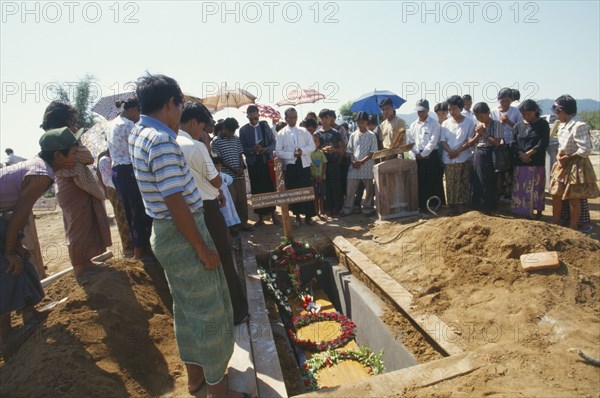 MYANMAR, Kachin State, Myitkyina, Jinghpaw Baptist funeral service with family gathered around grave near Prayer Mountain