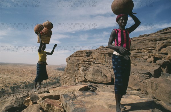 MALI, Bandiagara Cliffs, One woman carrying beer and another pots on their heads standing at the top of the Bandiagara Escarpment on their way to village market.