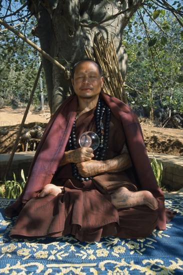 THAILAND, Wat Phra Acha Tong, Portrait of Buddhist monk from The Golden Horse Forest Monastery meditating in the lotus position beneath tree.