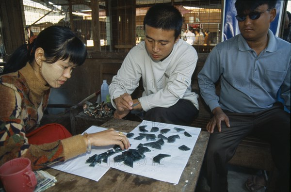 MYANMAR, Mandalay, Jade traders examining cut pieces in central jade market.