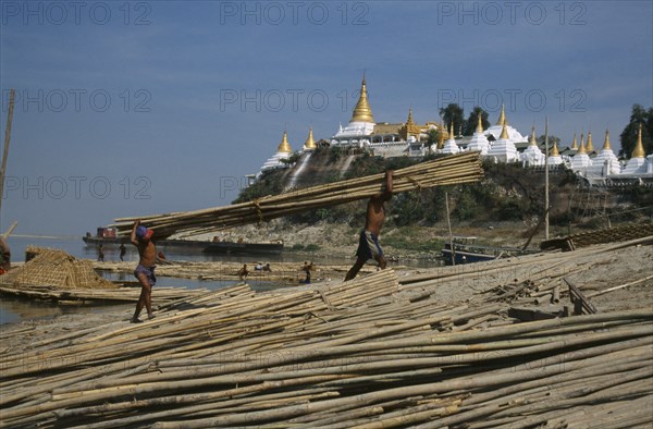 MYANMAR, Mandalay, Unloading lengths of cane on the banks of the Ayeyarawady overlooked by temple behind.
