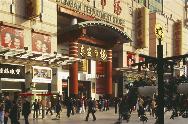 CHINA, Beijing, Wanfujing Dajie department store.  Entrance on to busy street with advertising covering exterior wall.