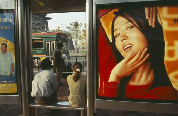 CHINA, Beijing, People waiting at bus stop south of Tiananmen Square with advertising hoarding covering exterior wall.