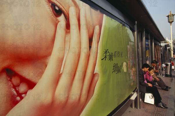 CHINA, Beijing, People waiting at bus stop south of Tiananmen Square with advertising hoarding covering exterior wall.