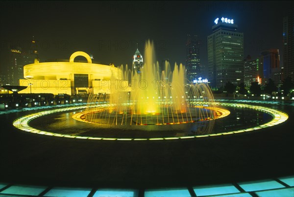CHINA, Shanghai, Shanghai Museum of Chinese culture built in the 1930s and converted to a museum in 1952.  Exterior and city buildings illuminated at night with fountain in foreground.