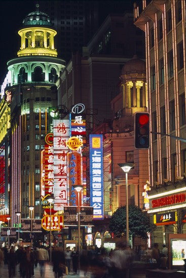 CHINA, Shanghai, Nanjing Road at night with illuminated neon signs and crowds of people in blurred movement below.