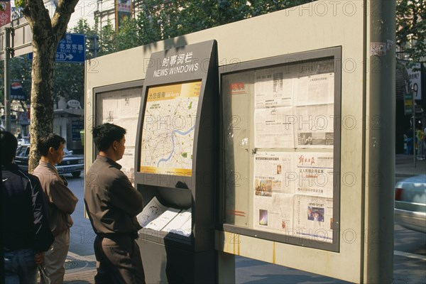 CHINA, Shanghai, Nanjing Road.  Men reading map and newspapers displayed on boards in ‘news windows’ on the street.