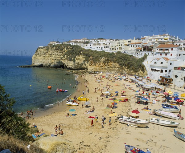 PORTUGAL, Algarve, Carvoeiro, White painted town on rocky headland overlooking busy beach.