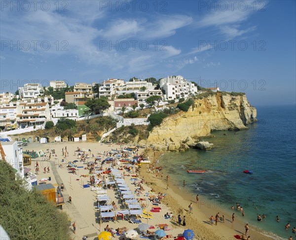 PORTUGAL, Algarve, Carvoeiro, White painted town on rocky headland overlooking busy beach.