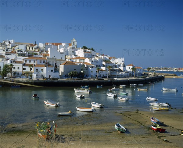 PORTUGAL, Algarve, Ferragudo, White painted town buildings overlooking harbour and moored boats.