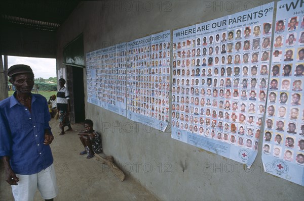 LIBERIA   , Margibi, Kakata, Man standing next to Red Cross tracing posters of Liberian children whose parents are missing