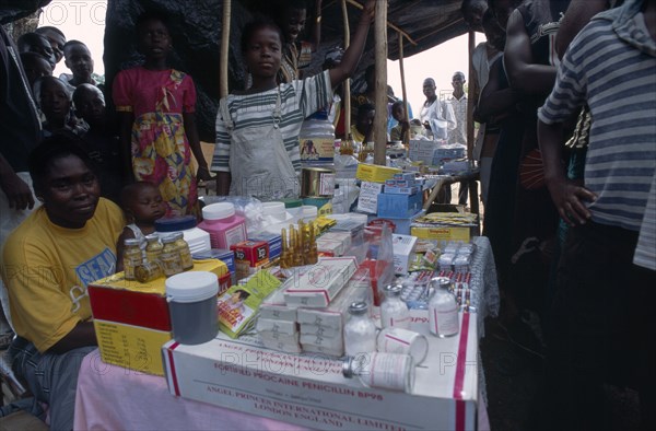 LIBERIA , Nimba, Saclepea, Woman behind stall with display of medical supplies surrounded by crowd of adults and children.