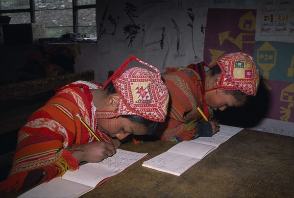 PERU, Andes, Cusco, "Tastayoc Village.  Quechua Indian children wearing traditional clothing, in school writing at desk."