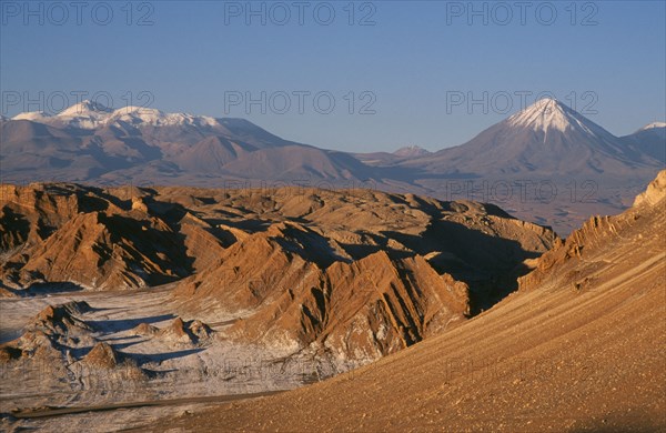 CHILE, Antofagasta, General, Salt deposits on desert surface near San Pedro de Atacama with snow capped peak of Volcano Lincancabur beyond.