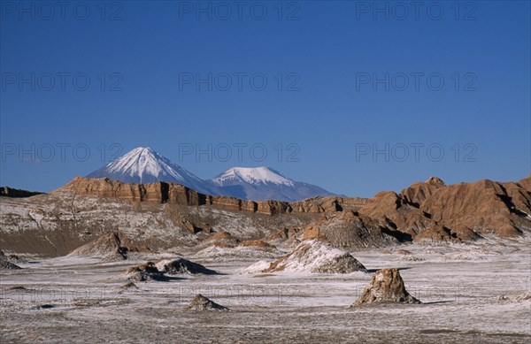 CHILE, Antofagasta, General, Salt deposits on desert surface near San Pedro de Atacama with snow capped peak of Volcano Lincancabur beyond.
