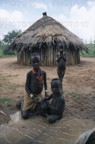 ETHIOPIA, Demeka, Hamer children sitting on animal skin outside thatched hut.