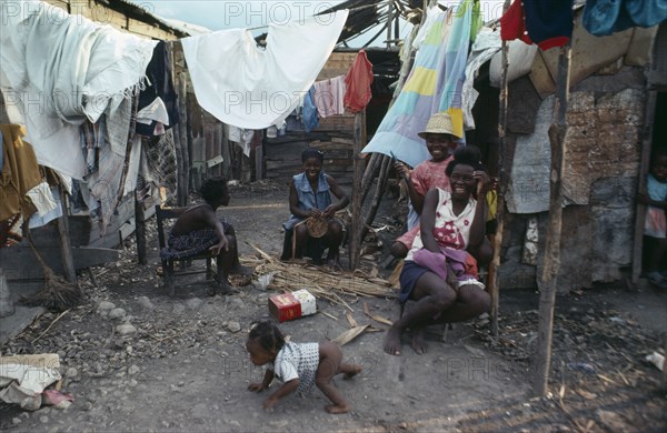 HAITI, People, Group of laughing women and children in shanty village sitting outside underneath washing line.