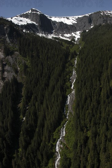USA, Alaska, Misty Fjords Nat. Monument, Snow capped mountain tops with waterfall running down steep tree covered slope