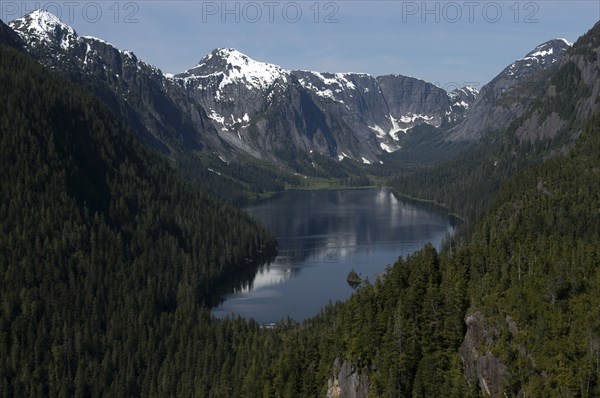 USA, Alaska, Misty Fjords Nat. Monument, View over lake with surrounding trees toward snow capped peaks