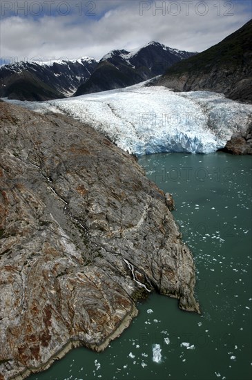 USA, Alaska, Tracy Arm Fjord, View over rocky edged waterway toward icy slope and mountain peaks beyond