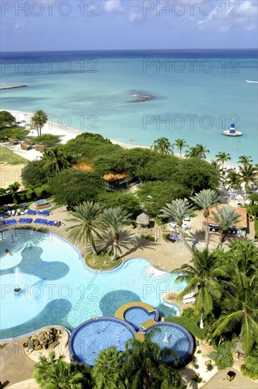 WEST INDIES, Dutch Antilles, Aruba, View over beach side hotel pool with clear blue sea beyond