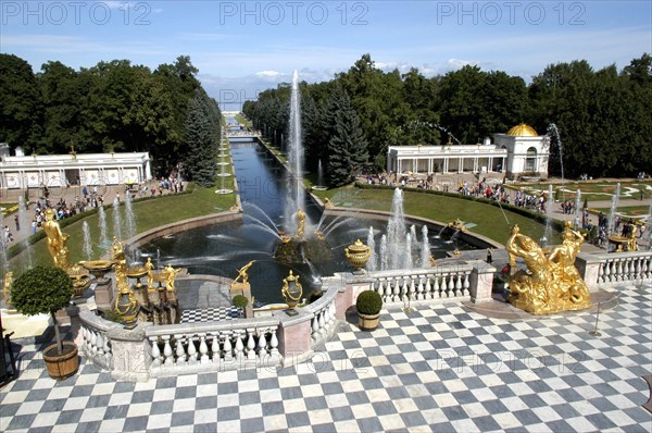 RUSSIA, Near St Petersburg, Peterhof Palace gardens. Stone balcony with chequered floor and golden statues with fountain beyond. Peterhof is also known as Petrodvorets.
