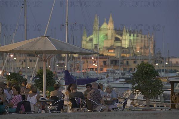 SPAIN, Balearic Islands, Majorca , Waterfront cafe at dusk in Palma de Mallorca with La Seo Cathedral in the background.