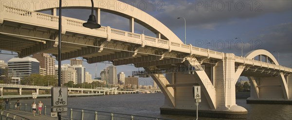 AUSTRALIA, Queensland, Brisbane, Walkers strolling along the River Walk beneath a road bridge over the Brisbane River.