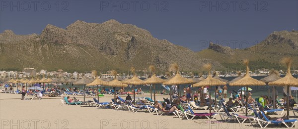 SPAIN, Balearic Islands, Majorca, "Sun loungers, tourists and parasols on the beach at Puerto de Pollensa."