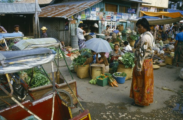 INDONESIA, Toraja, Market with sellers sitting around baskets of green vegetables with a market overseer looking on.