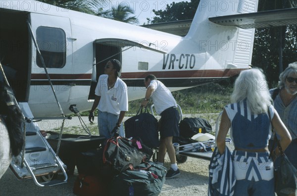 WEST INDIES, Cayman Islands, Little Cayman, Passenger plane with tourists on runway unpacking luggage.