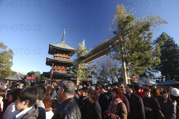JAPAN, Honshu, Chiba , "Narita San Temple. New Years Holiday worshippers crowd the front court of the temple with the pagoda and traditional gate of pine, bamboo and bundled rice straw behind "