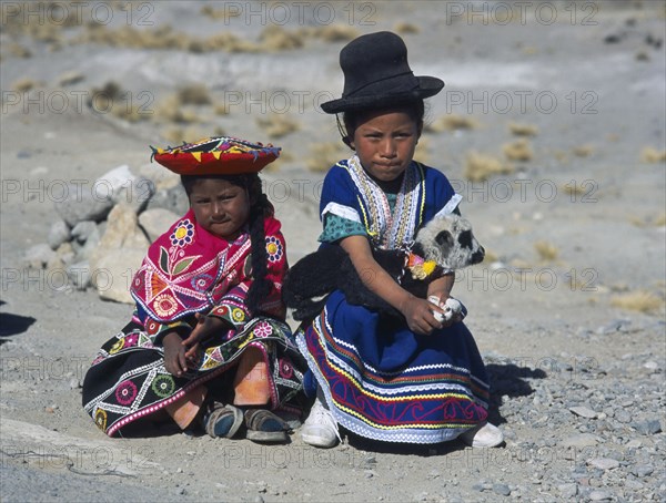 PERU, Near Arequipa, Two young children sitting on the ground with one holding a lamb