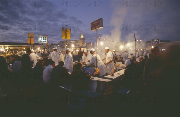 MOROCCO, Marrakesh, Djemaa el Fna. Food vendors serving up food to hungry customers seated around them at dusk