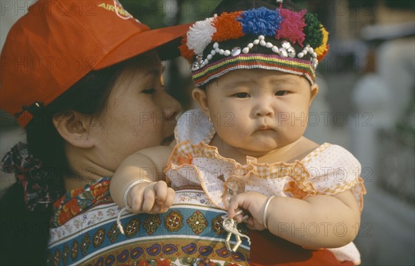 LAOS, Luang Prabang, Mother holding child dressed for New Year celebrations.