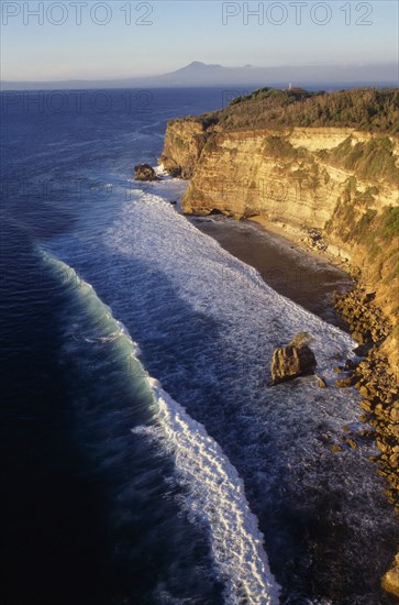 INDONESIA, Bali, Coastline, View north at sunset from Uluwatu Temple along rocky coastline towards distant volcano craters.