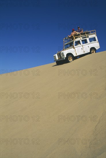 NAMIBIA, Skeleton Coast, Terrace Bay, Dune driving on the Roaring Dunes with jeep on crest of dune.