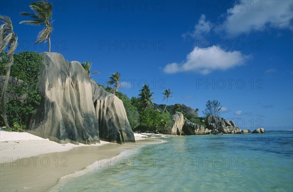 SEYCHELLES, La Digue, Anse Source d’Argent, Narrow stretch of empty sandy beach with large outcrops of rock and lush vegetation.