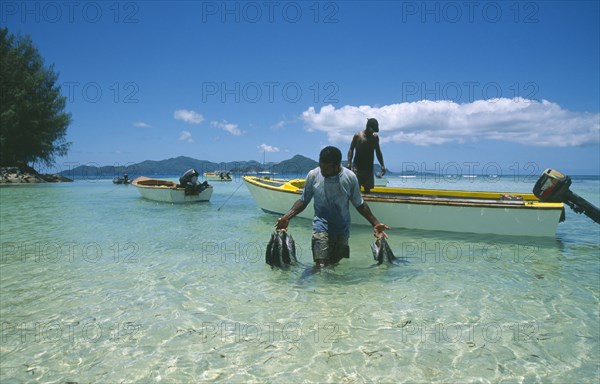 SEYCHELLES, La Digue, Fisherman wading ashore holding his catch.