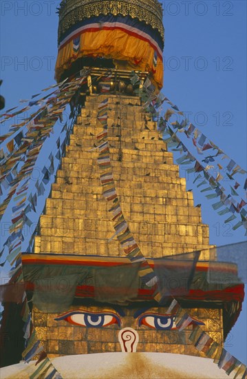 NEPAL, Kathmandu, Bodnath Stupa, Detail of spire of stupa with painted eyes and hung with prayer flags.